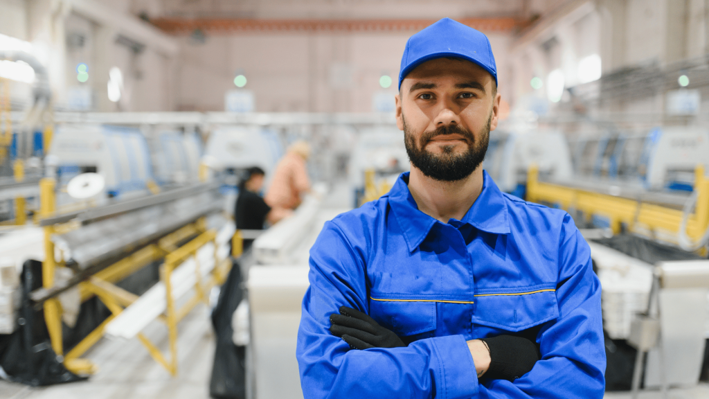 Pracownik produkcyjny w niebieskiej odzieży roboczej stojący na hali produkcyjnej przy nowoczesnej linii technologicznej